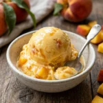 Bowl of homemade peach ice cream topped with fresh slices and mint leaves.
